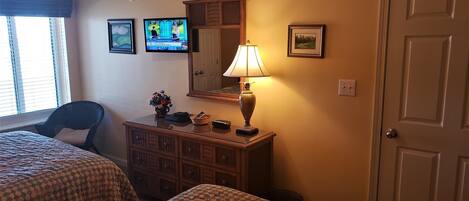 A hotel room with two beds, a dresser, a lamp, a television, and a door.