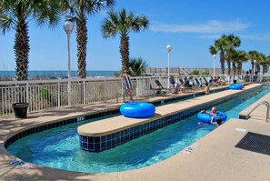 A pool area with a clear view of the ocean, lounge chairs, and palm trees. - Crescent Shores - Amenity Filled, Great Oceanfront Views from large balcony (North Myrtle Beach)