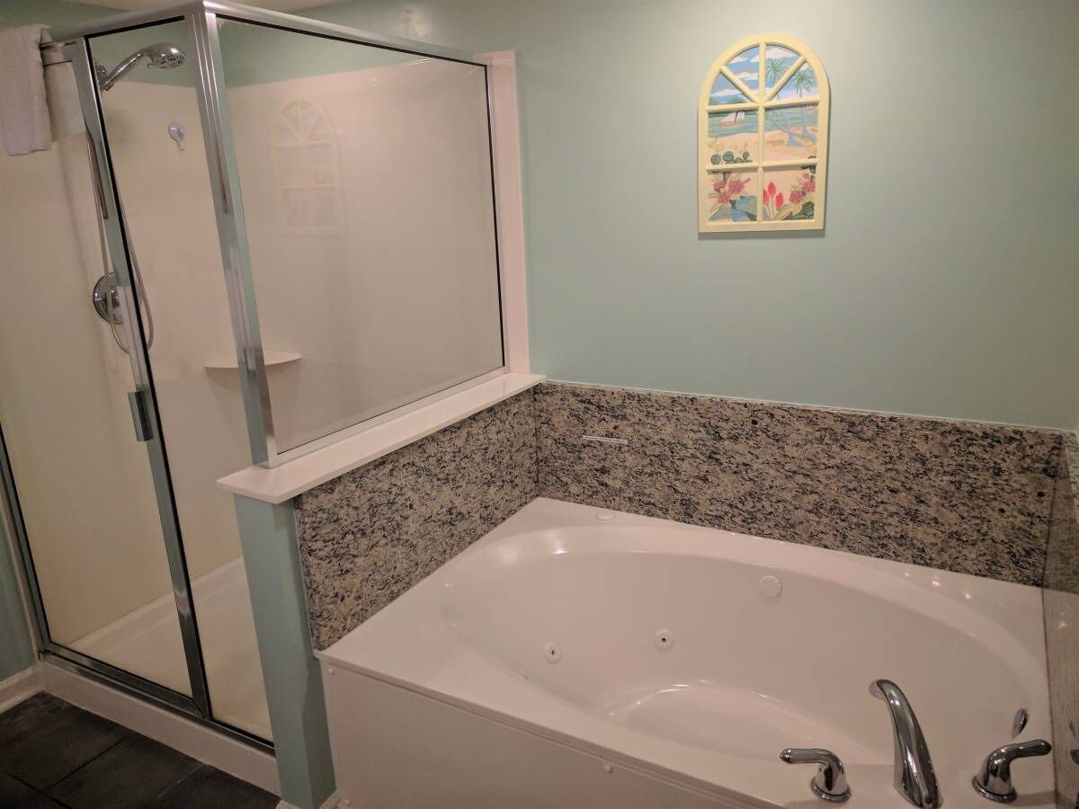 Een badkamer met een douchecabine van glas, een vrijstaand bad en een decoratief raam met uitzicht op een strand.
