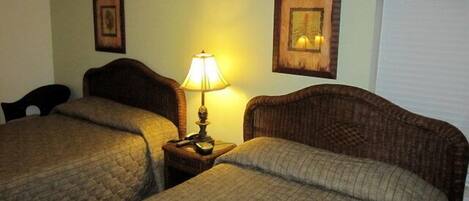 A hotel room with two beds, a nightstand with a lamp, and two framed pictures on the wall.