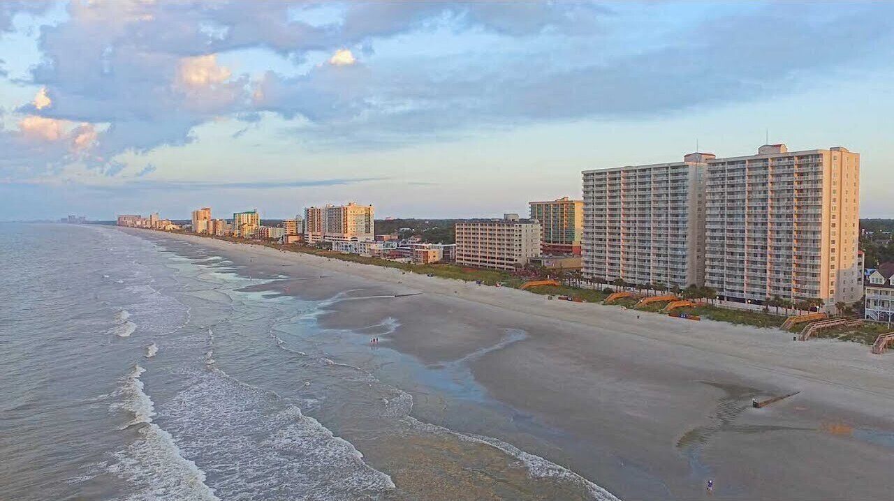 Un hotel costero con varios edificios altos, una playa y cielo despejado.