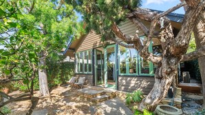 Una casa con veranda in vetro, gradini in pietra e un grande albero nel giardino.