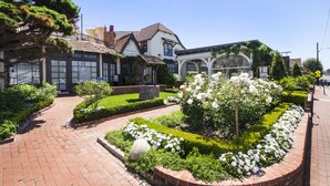 Un edificio tradizionale con facciata in mattoni, ampie finestre e un giardino curato con fiori bianchi e siepi.