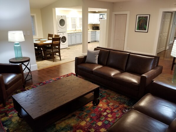 A living room with a brown leather sofa, a wooden coffee table, and a colorful rug.