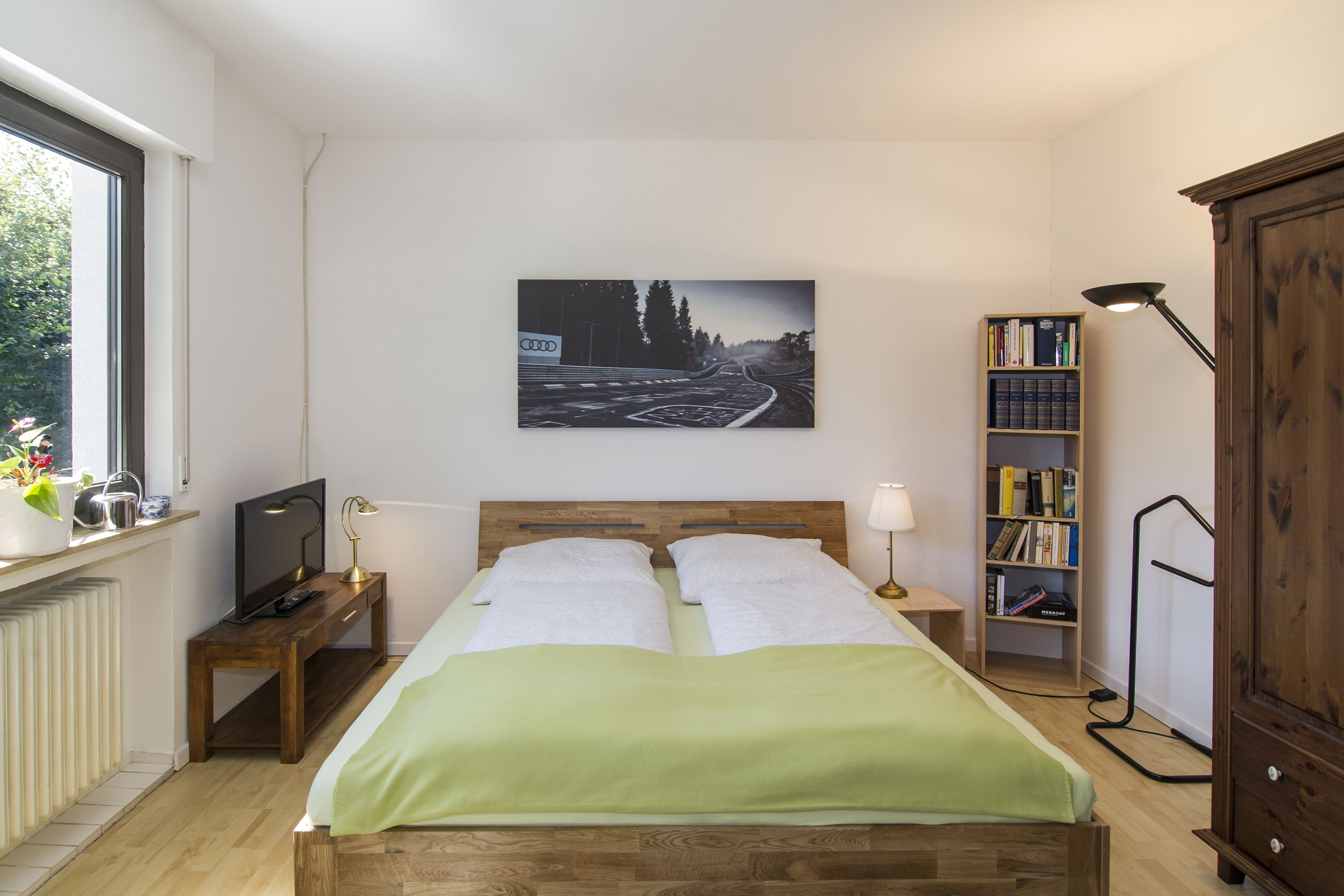 Quarto com cama, televisão, estante e janela.