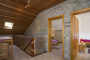 A loft bedroom with a sloped ceiling, wooden beams, a stone wall, a wooden staircase, and a bed with a pink mattress. - Ferienhaus Faltmann (Heimbach)