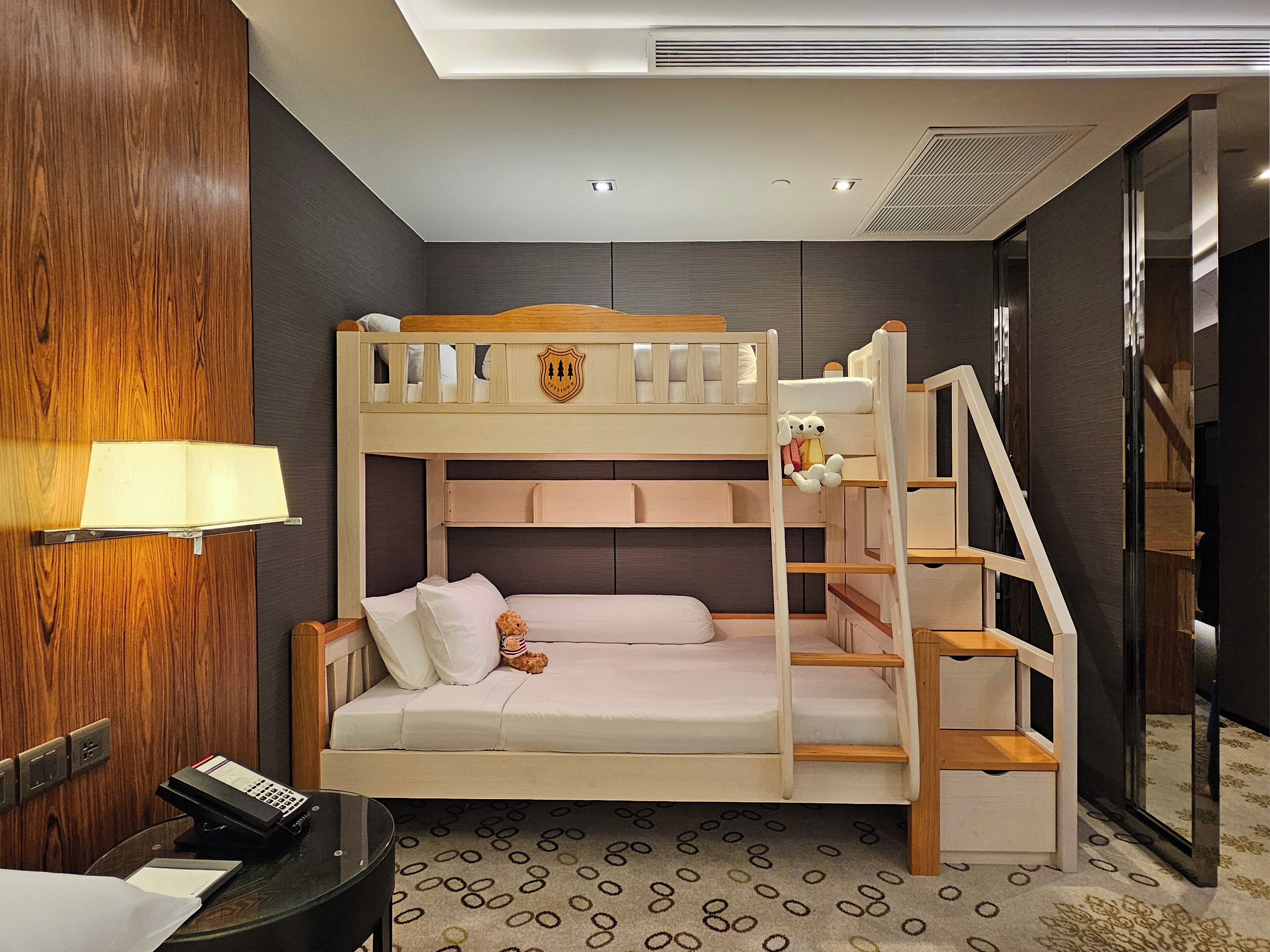 A bunk bed with a desk and lamp, a teddy bear, and a patterned carpet.
