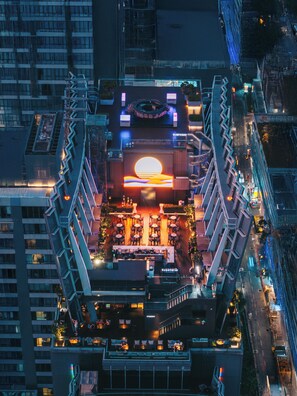 Un restaurant situé sur le toit d’un immeuble, doté d’une installation centrale représentant le soleil, de places assises en plein air et offrant une vue sur le paysage urbain.