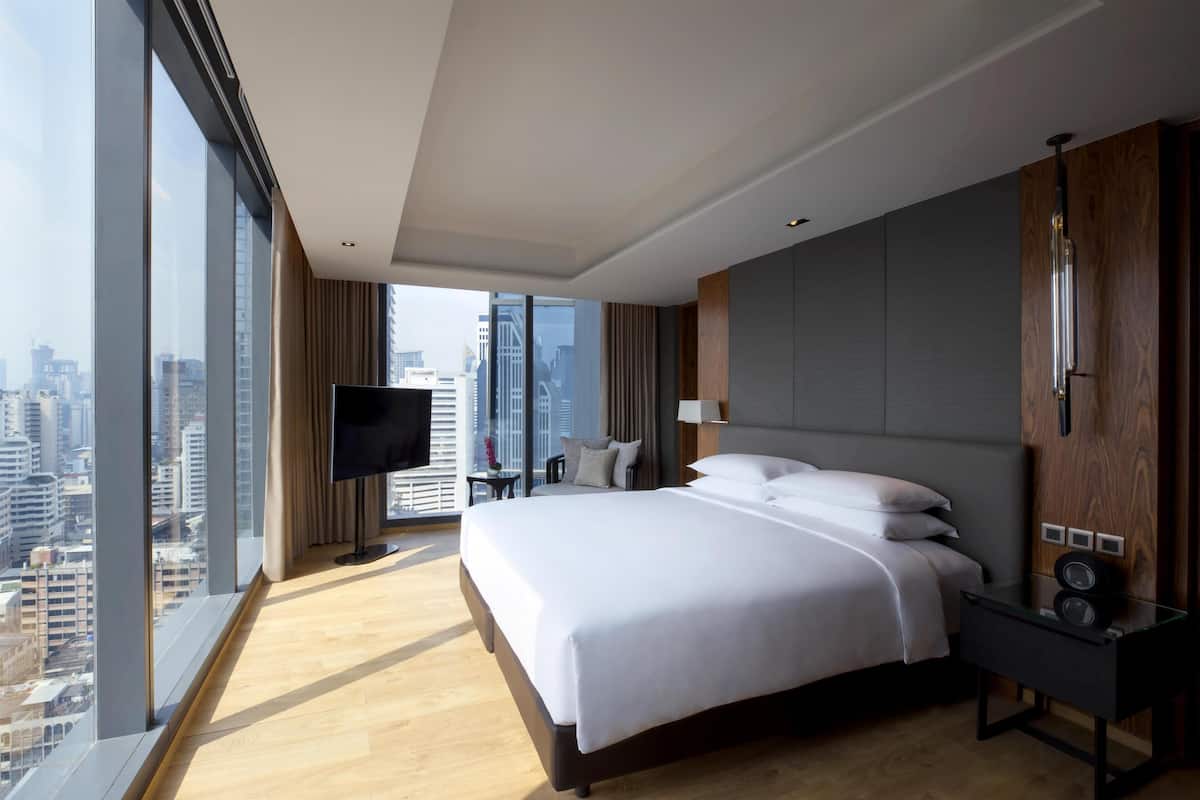 Une chambre d’hôtel moderne dotée d’un grand lit, d’une télévision à écran plat, d’une table de chevet et offrant une vue sur la ville.