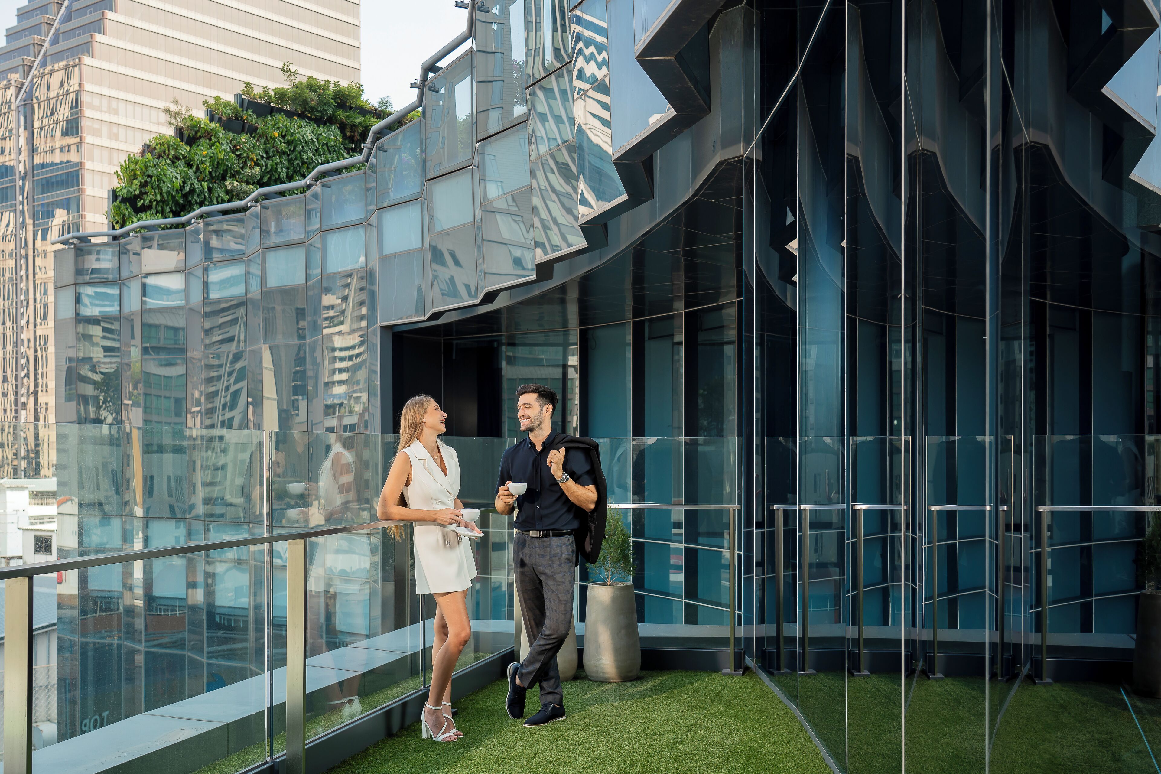 Un bâtiment moderne doté de grandes fenêtres en verre réfléchissant et d’un jardin sur le toit.