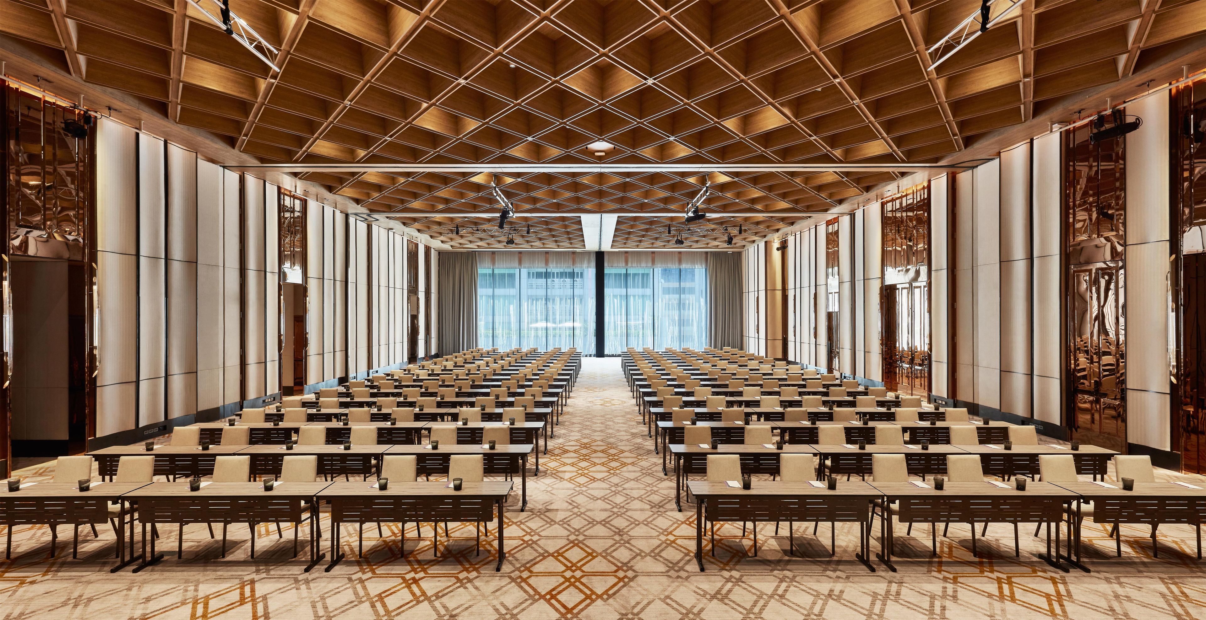 A conference room with rows of tables and chairs, a patterned carpet, and a wooden ceiling with a grid design.