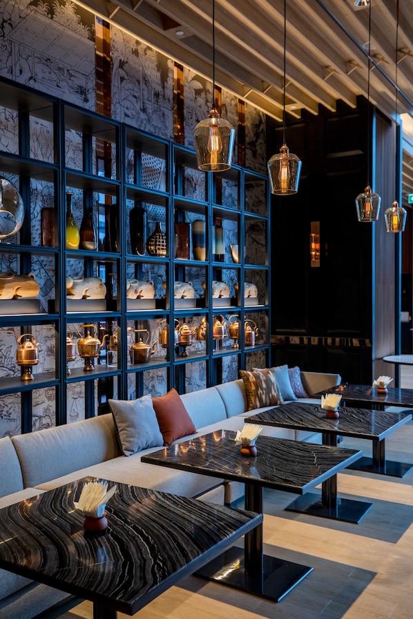 Un interior moderno con una zona de estar, estanterías decoradas y lámparas colgantes.