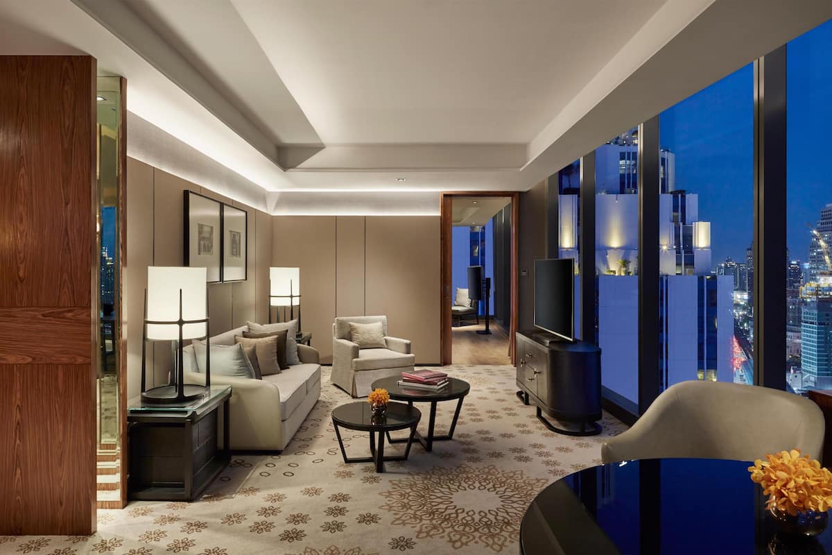 Une chambre d’hôtel avec un canapé, une table basse, une télévision, une lampe et une vue sur le paysage urbain.