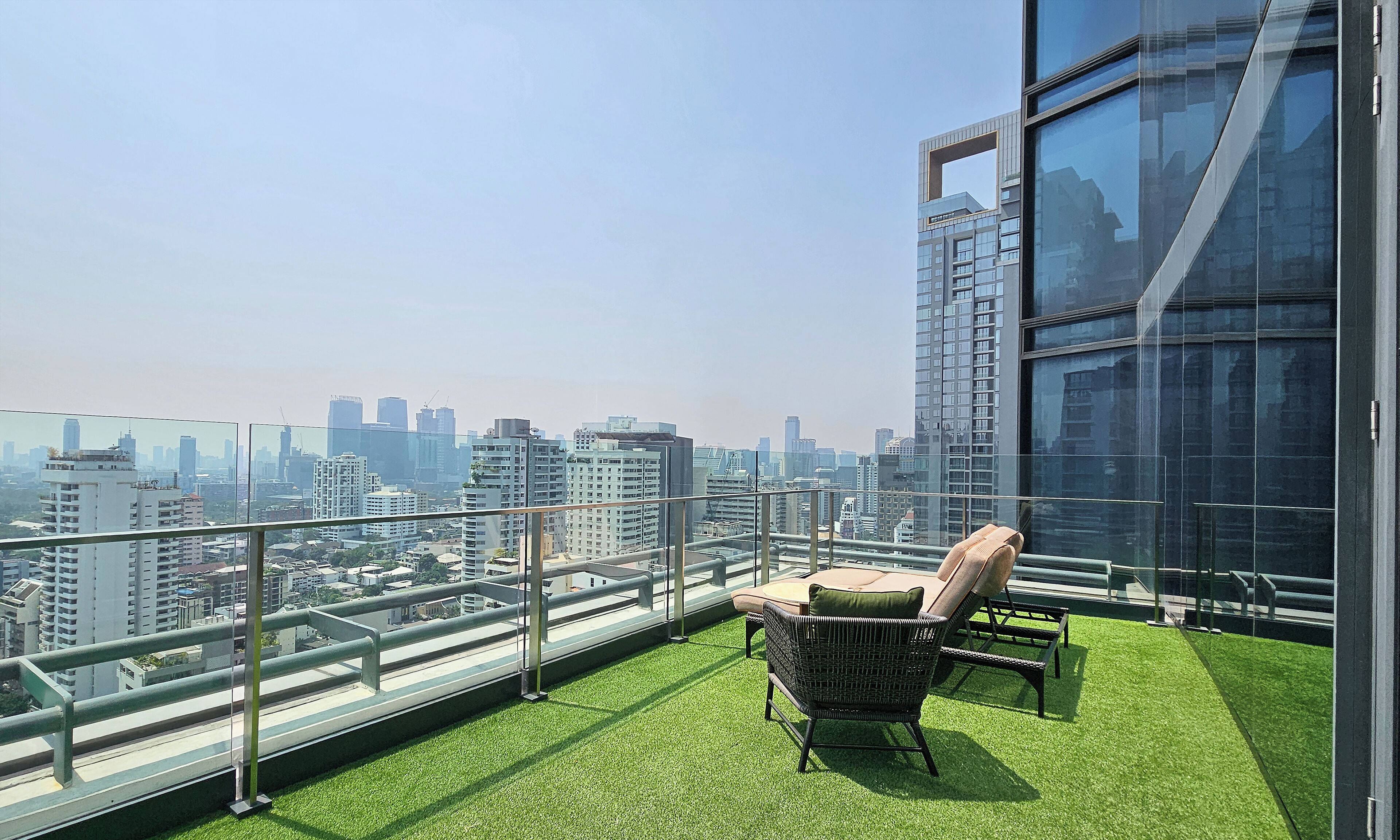 A balcony with artificial grass, two wicker chairs, and a city view.