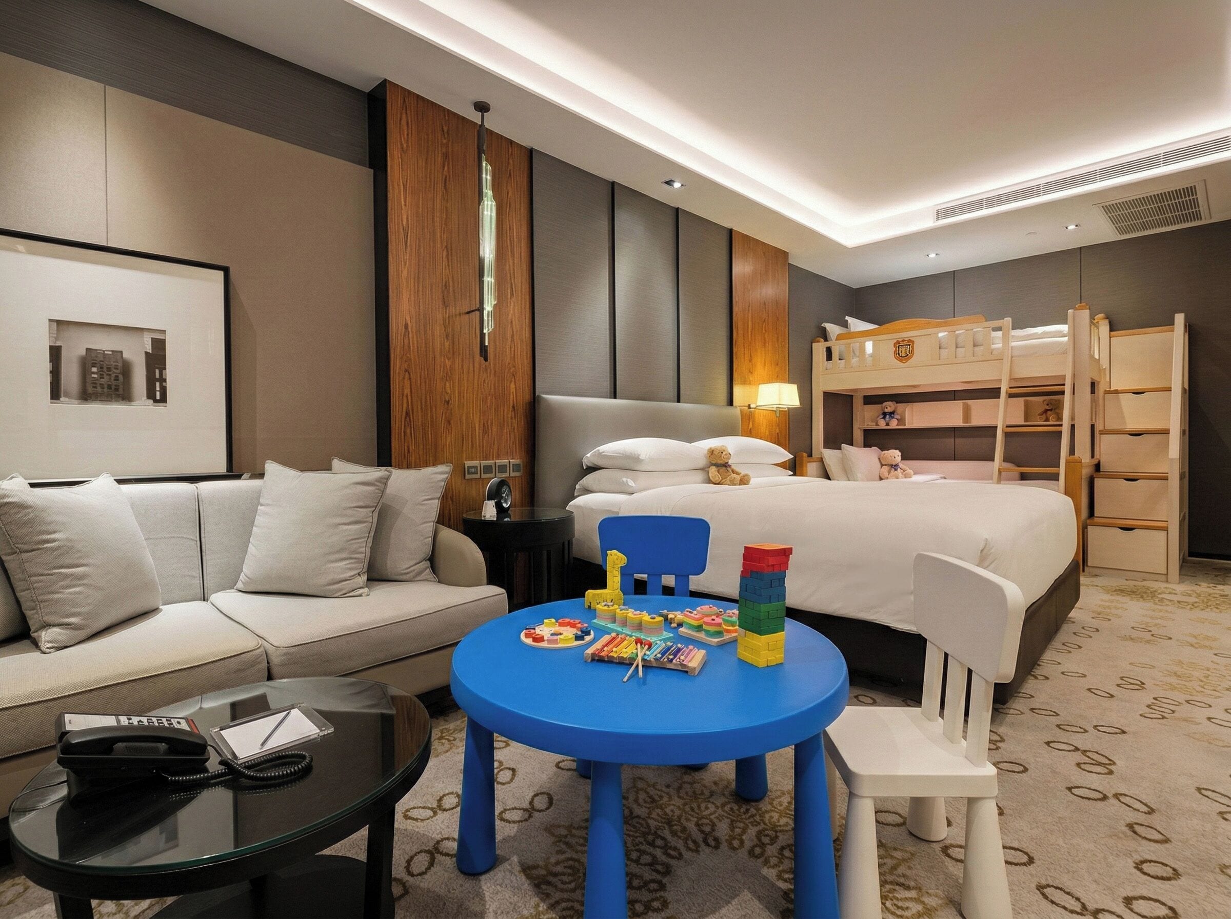 A hotel room with a bed, a sofa, a small table with toys, and a bunk bed.