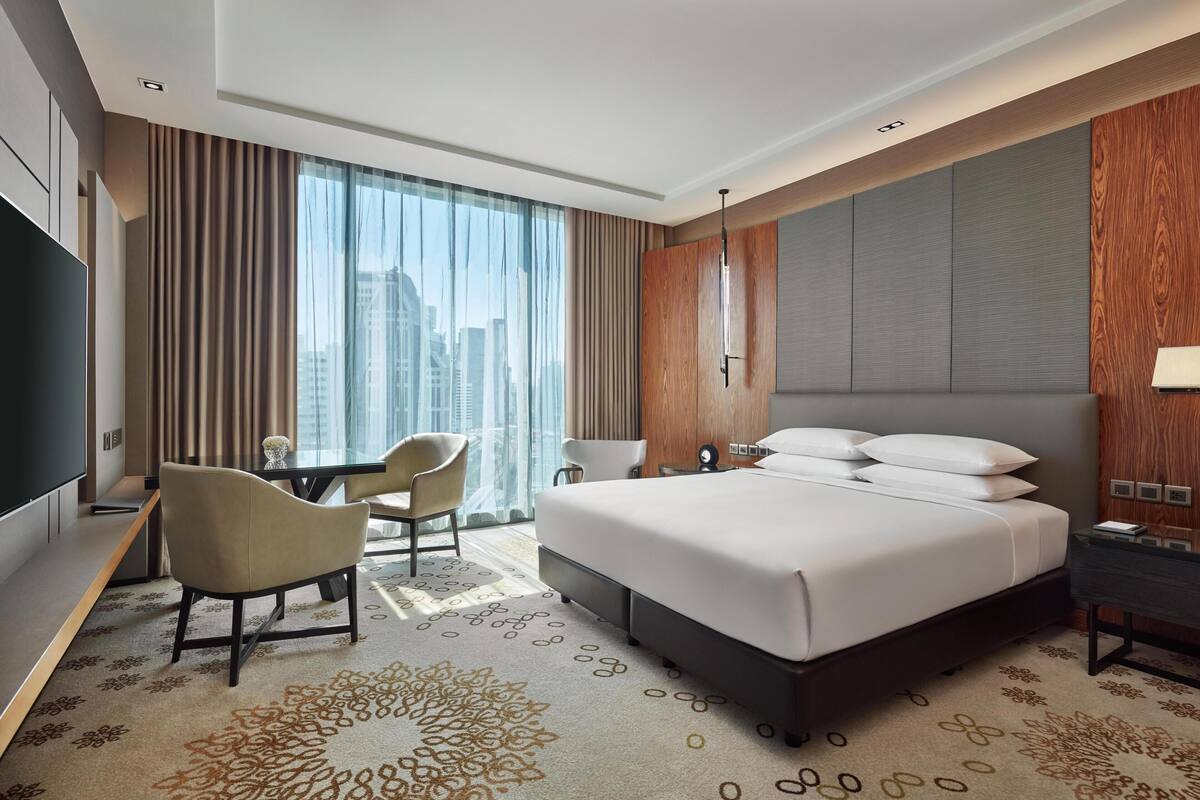 Une chambre d’hôtel avec un grand lit, deux fauteuils, un bureau, une télévision et une vue sur la ville.