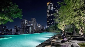 Une piscine sur le toit, dotée de chaises longues, avec une vue sur les toits de la ville illuminée la nuit.