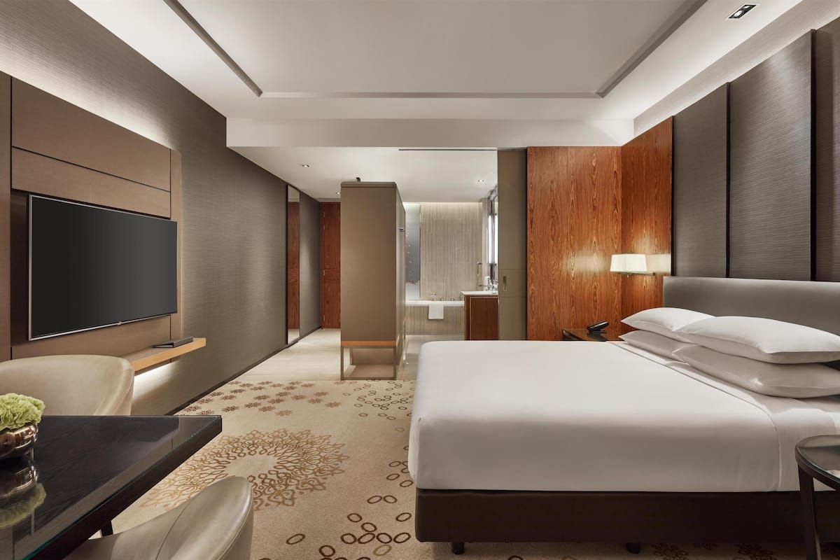 Une chambre d’hôtel avec un lit, une télévision, un bureau et une salle de bain, visibles à travers une porte ouverte.