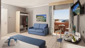A hotel room with a bed, a blue sofa, a dining table with chairs, a balcony with a view of the sea, and a TV mounted on the wall.