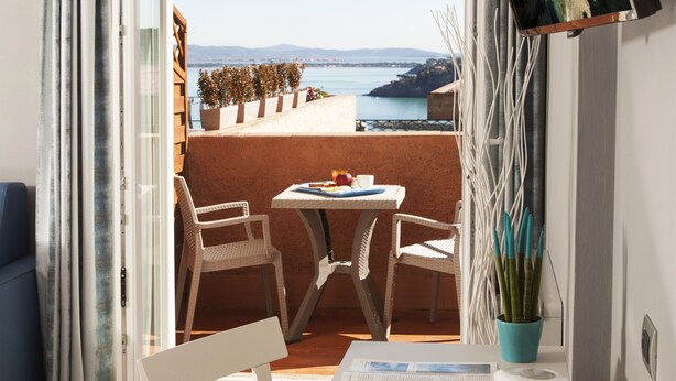 A room with a balcony, a table with a tray of items, and a view of the sea. - Bike&Boat Argentario Hotel (Monte Argentario)