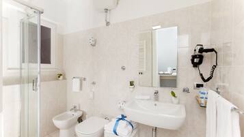 Ein modernes Badezimmer mit einer Duschkabine aus Glas, einem Bidet, einer Toilette, einem Waschbecken und einem an der Wand befestigten Föhn.