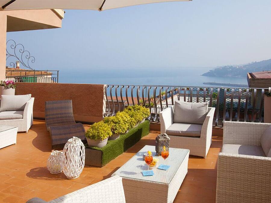 A terrace with wicker furniture, a small table with drinks, and a view of the sea.