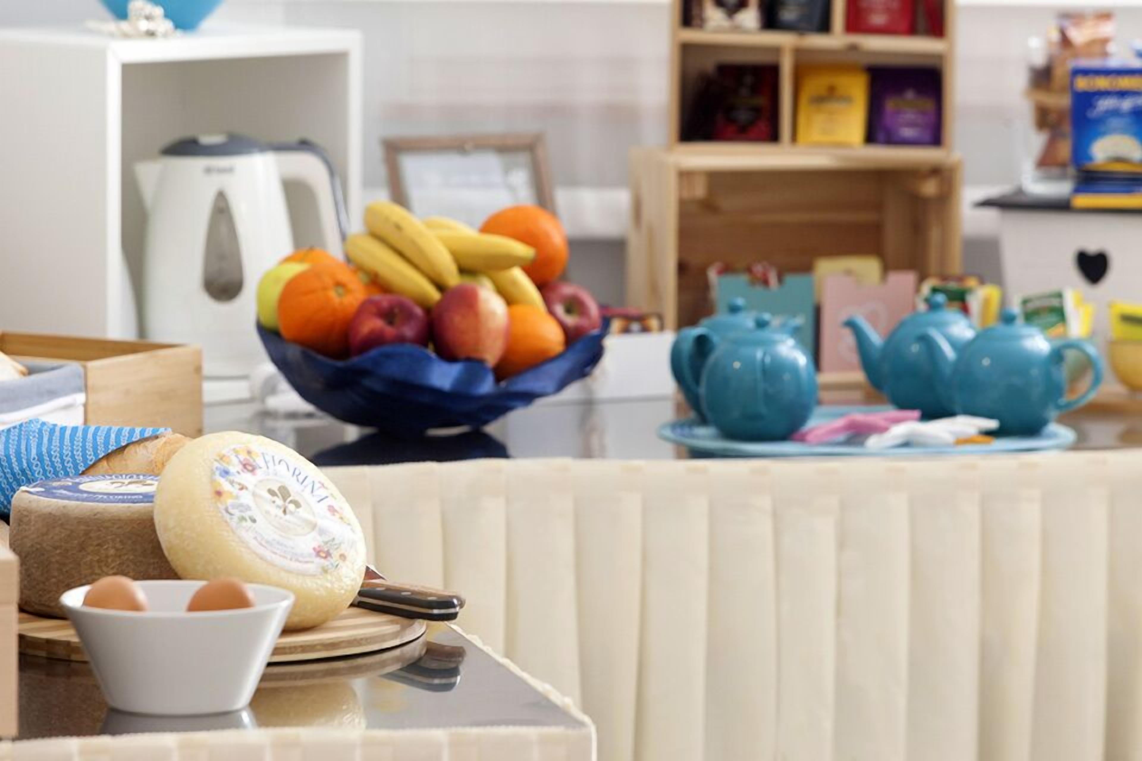 A breakfast setting with a fruit bowl, cheese, eggs, and teapots on a table.