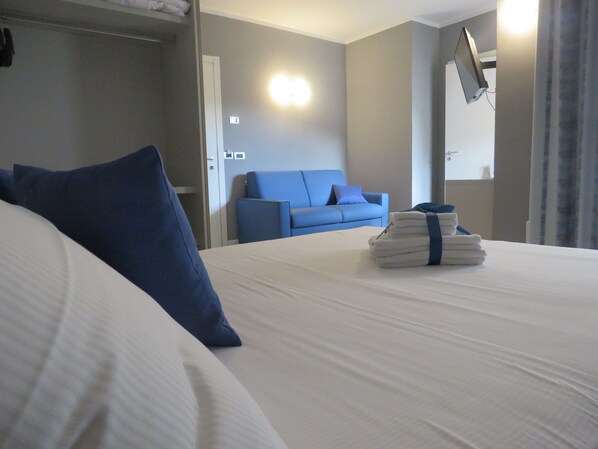 Habitación de hotel con una cama, un sofá azul, un televisor montado en la pared y una pila de toallas sobre la cama.
