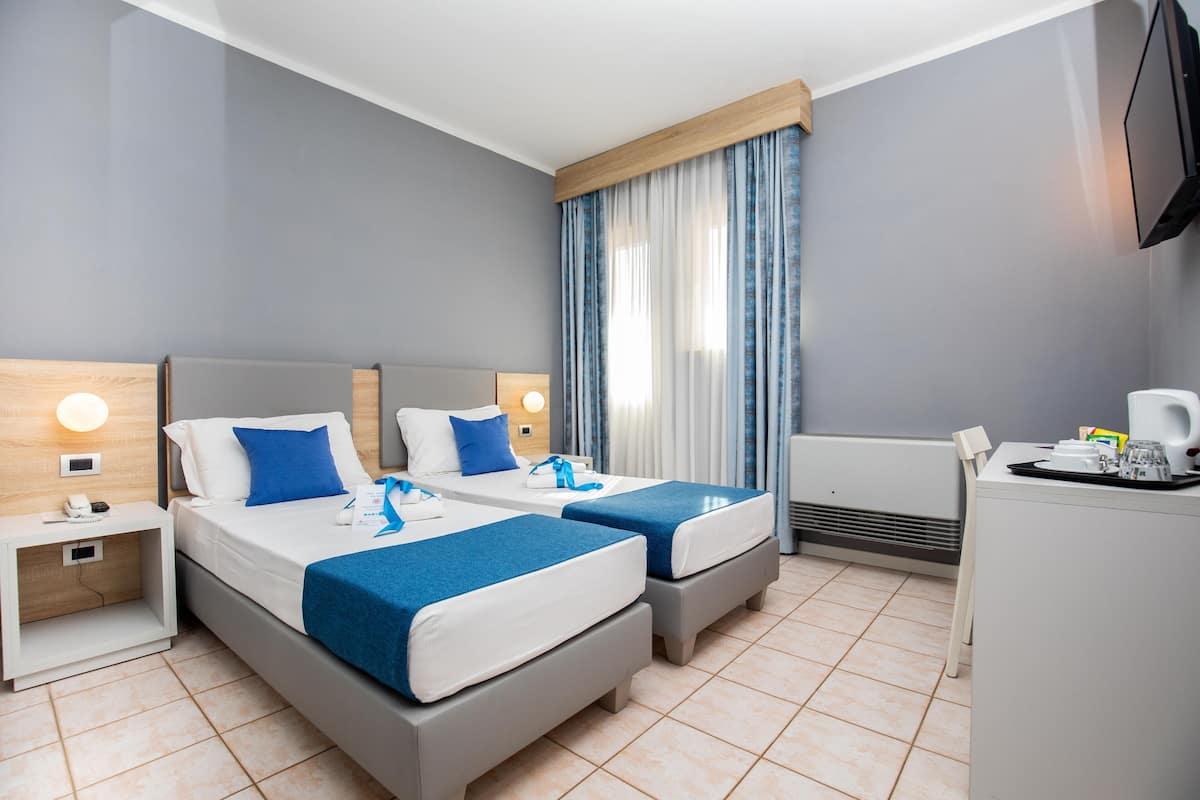 A hotel room with two beds, a desk, a chair, a TV, and a window with curtains.