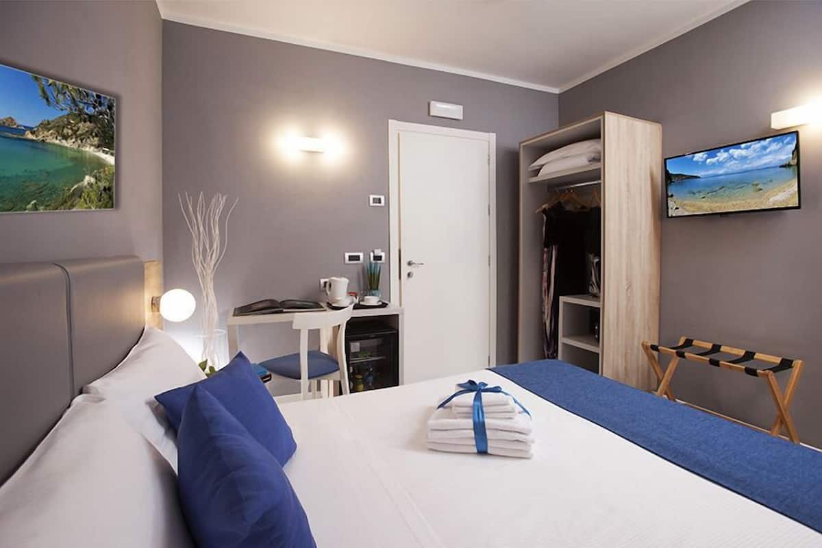 A hotel room with a bed, a desk, a chair, a wardrobe, and a TV.