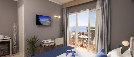A hotel room with a bed, a television, a balcony with a table and chairs, and a view of the sea.