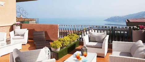A terrace with wicker furniture, a coffee table, and a view of the sea.