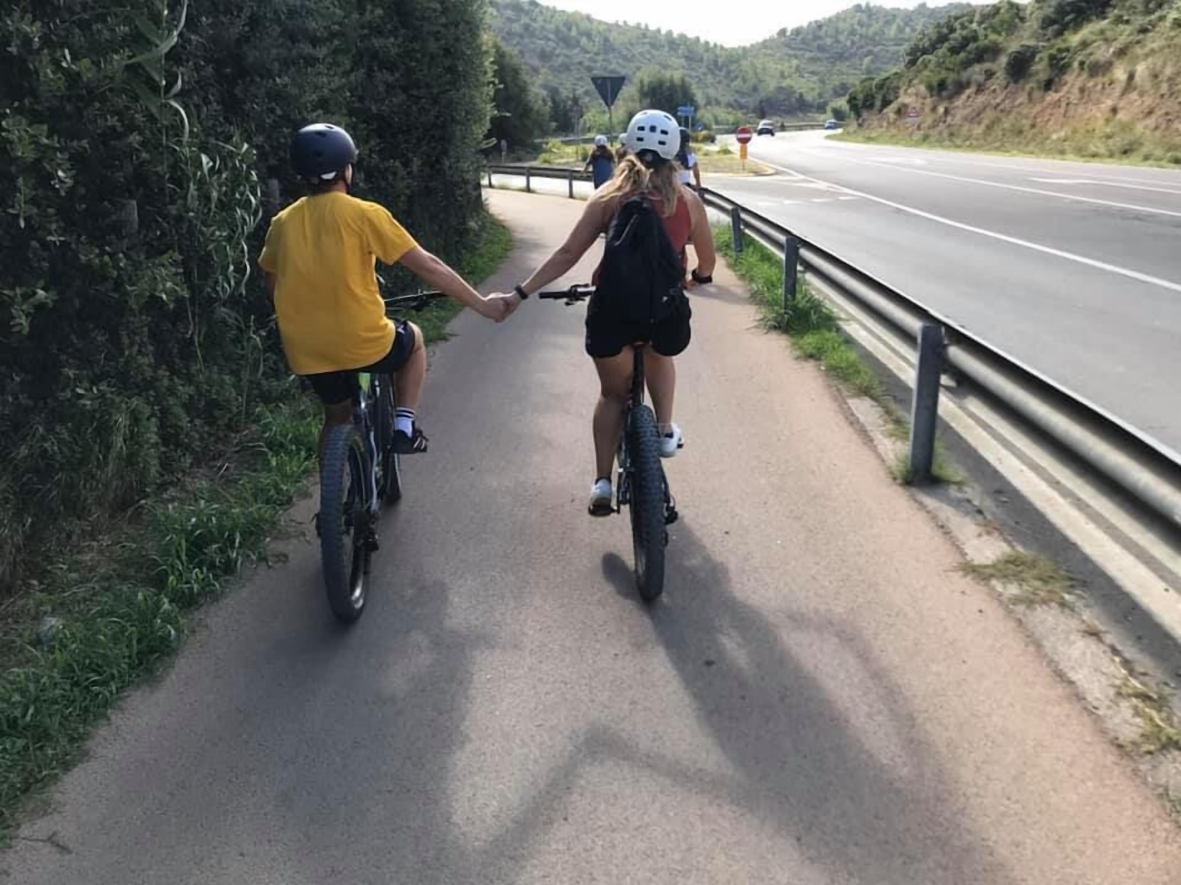 Two people on bicycles on a paved path alongside a road.