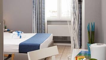 Habitación de hotel con una cama, una mesa de comedor con una bandeja de tazas y platillos blancos, una silla y una ventana con cortinas.