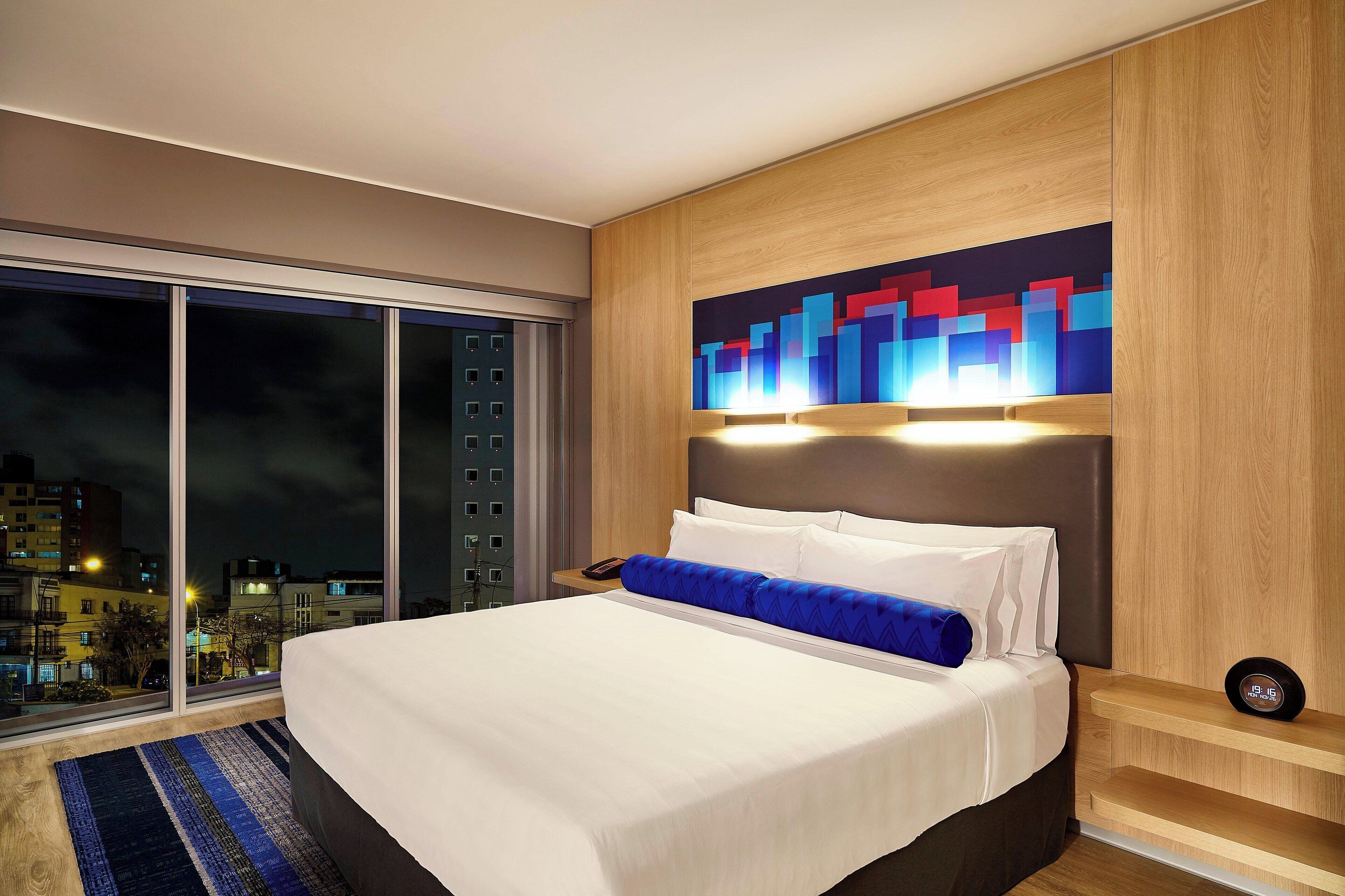 Una habitación de hotel moderna con una cama grande, vistas a la ciudad y un cabecero de madera.