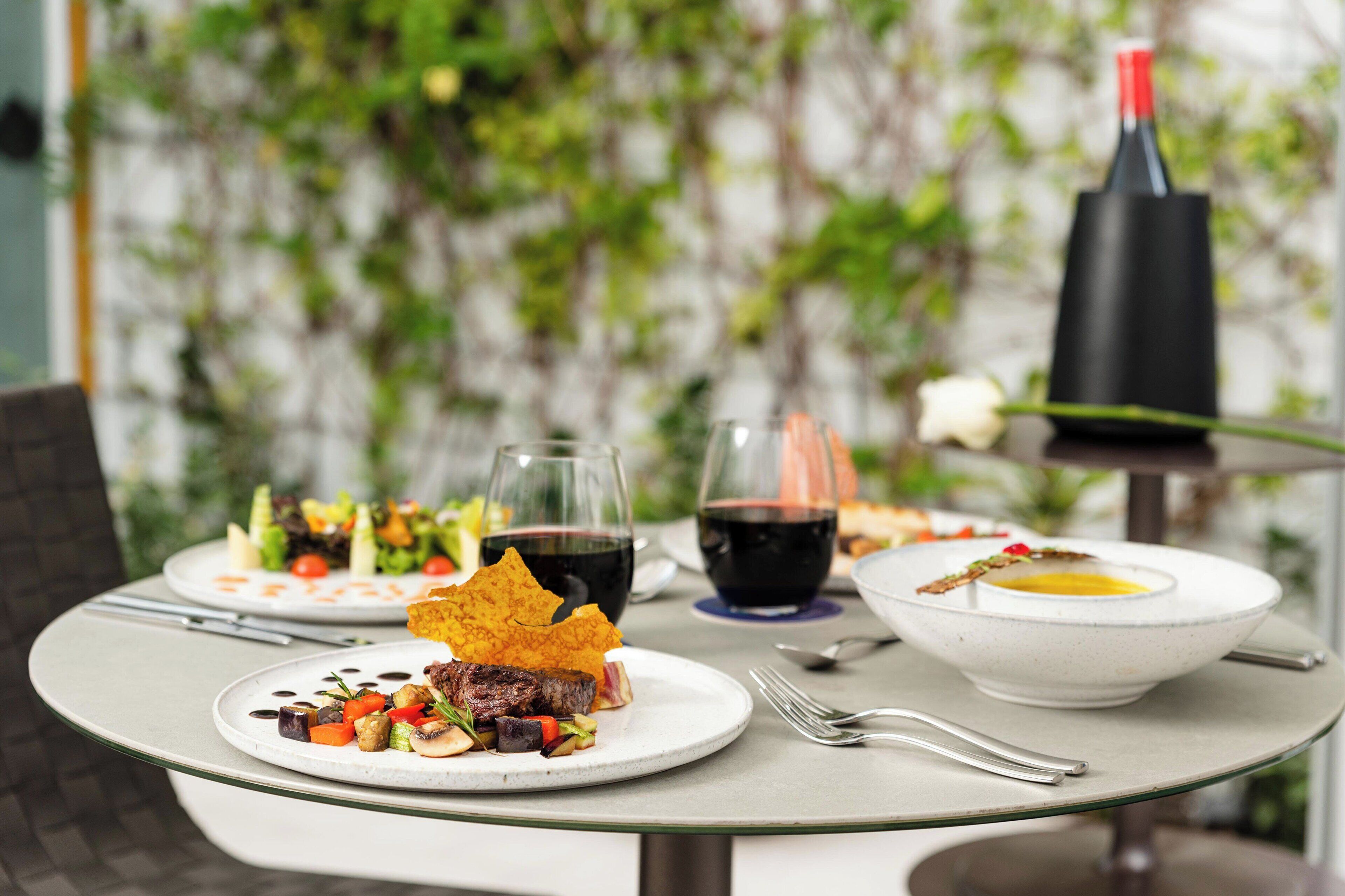 A dining table with plates of food, two glasses of red wine, and a bottle of wine.