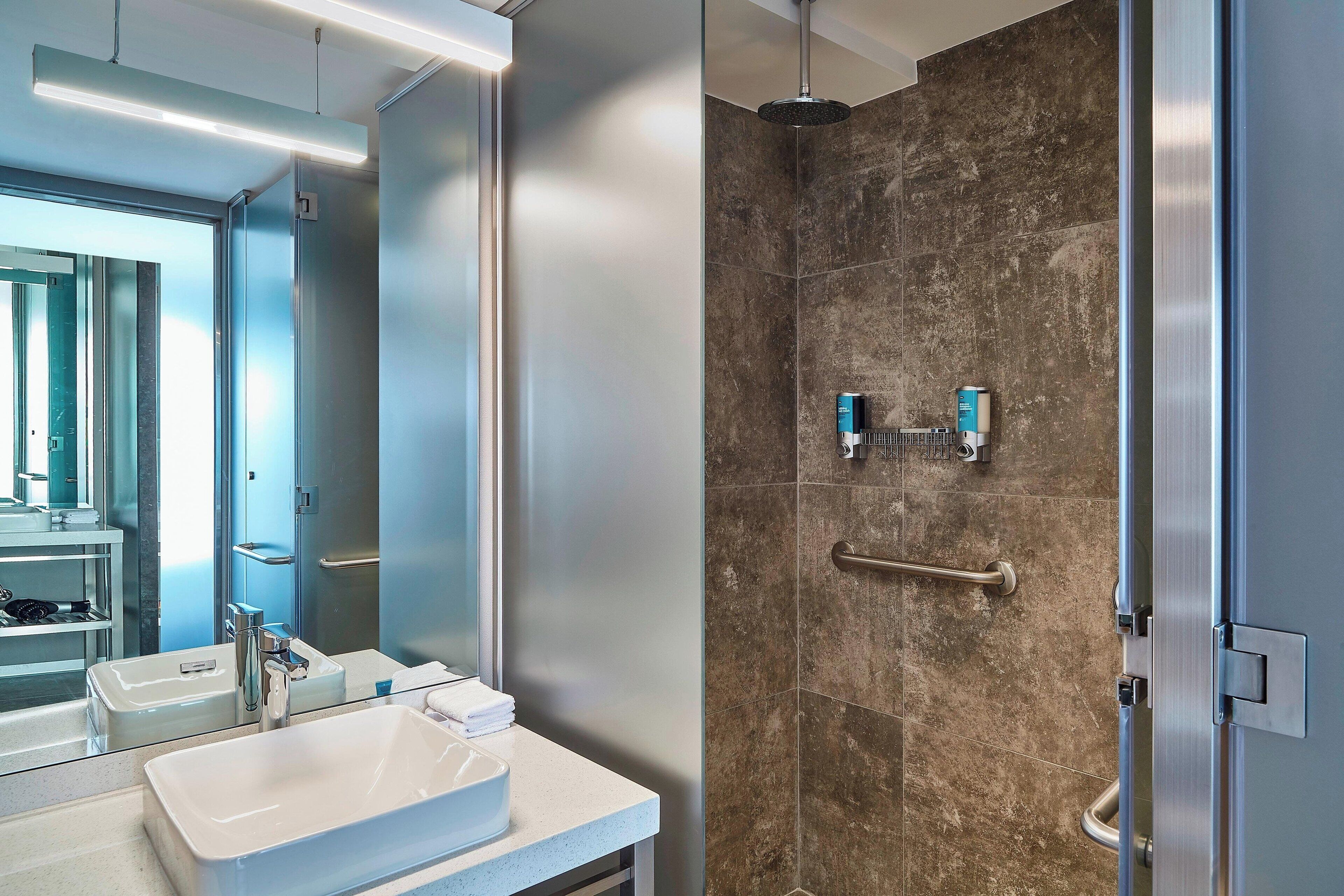 A modern bathroom with a large mirror, a white sink, and a shower area with a glass door.