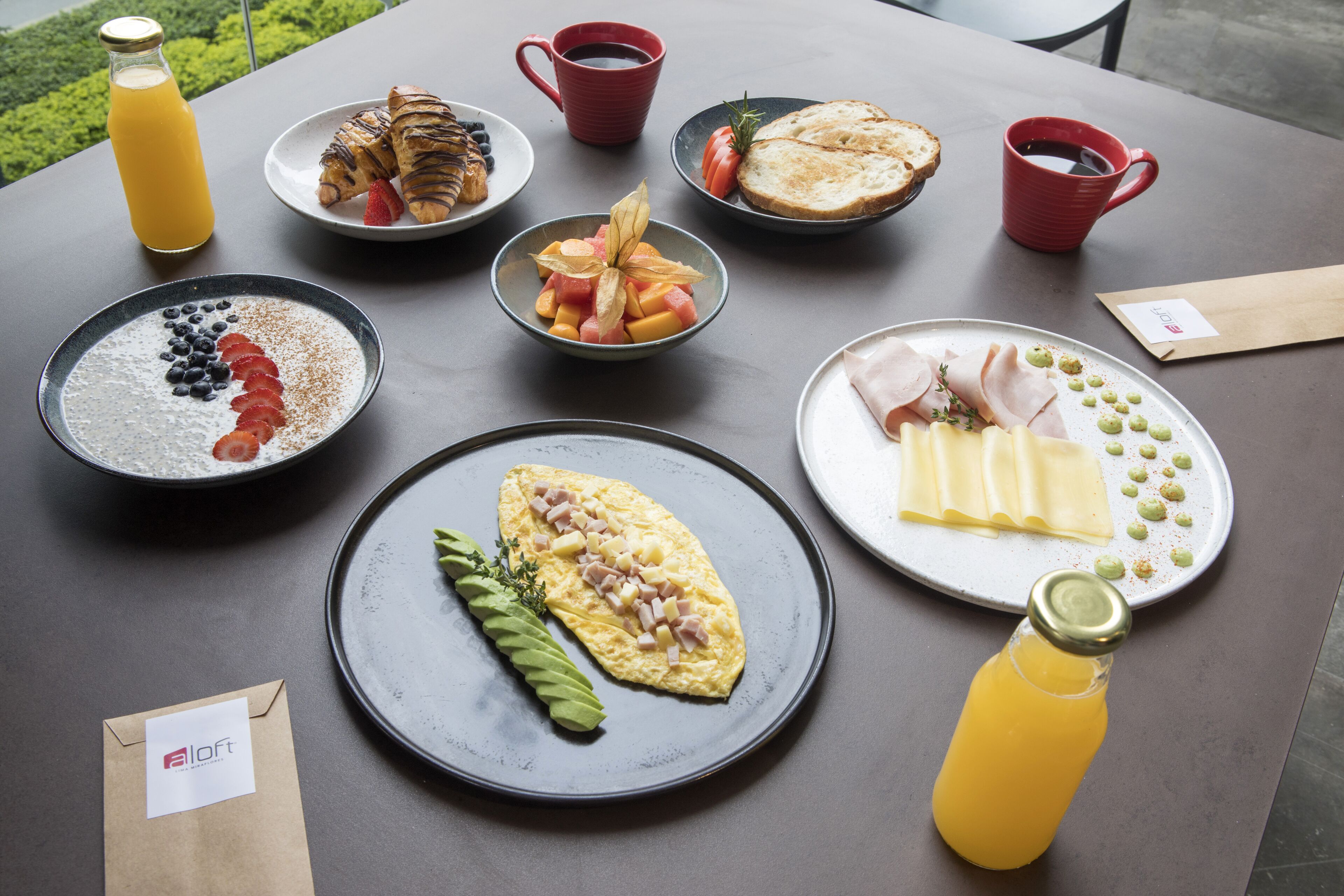 Ein Frühstückstisch mit verschiedenen Speisen, darunter Toast, Obst und einer Platte mit Schinken und Käse.