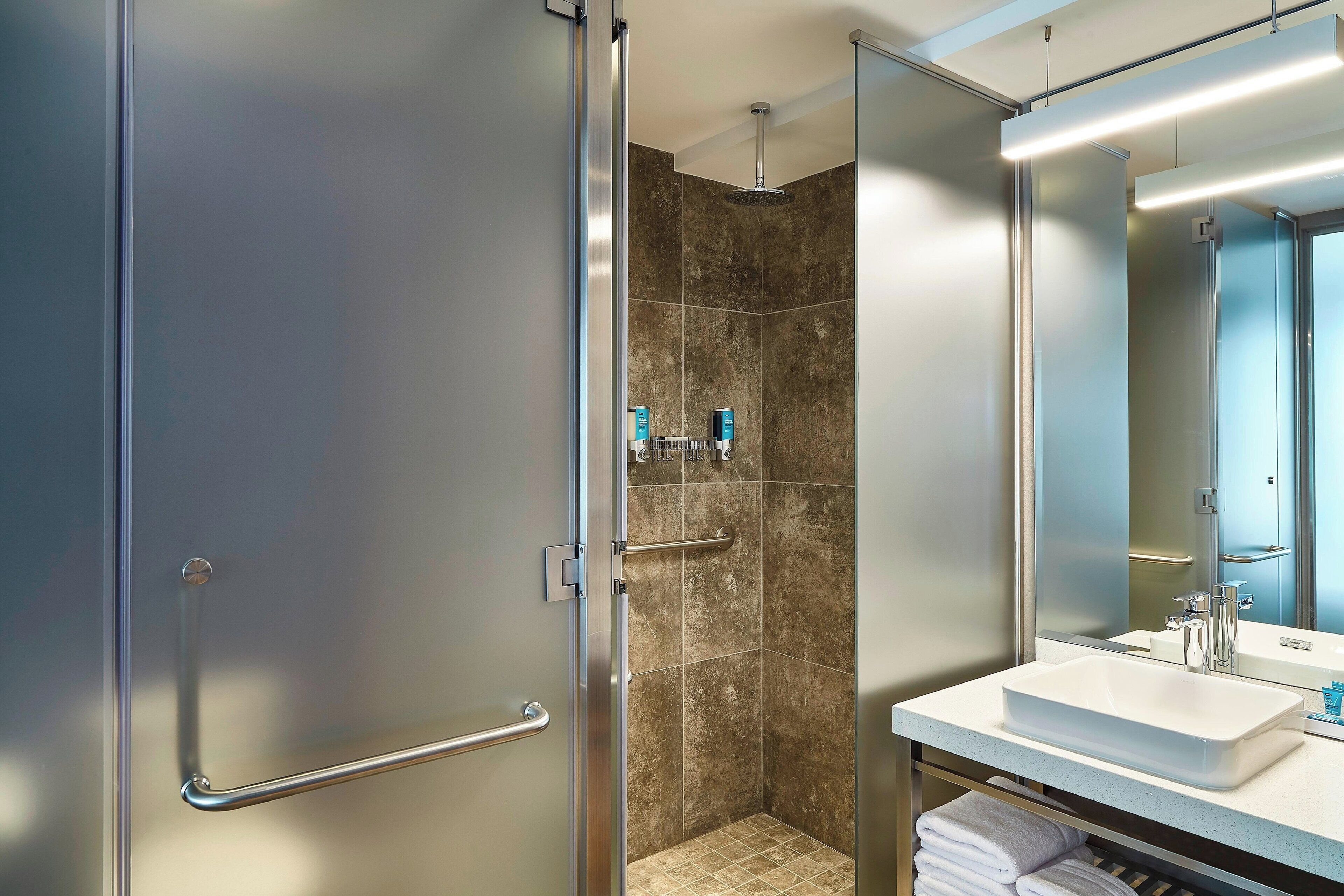 A modern bathroom with a glass shower enclosure, a white sink, and a large mirror.