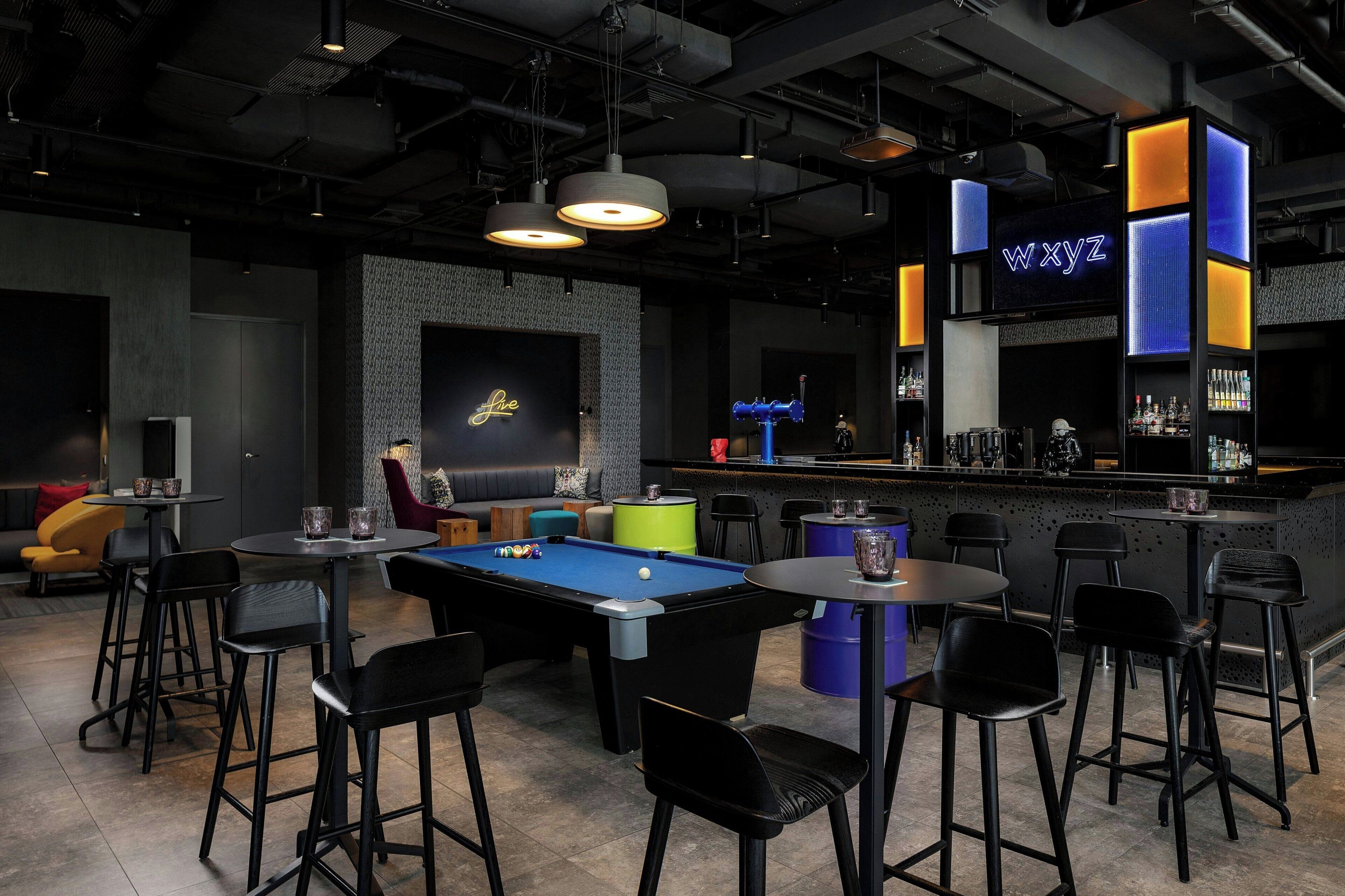Zona de bar con mesa de billar, taburetes y un letrero de neón que dice "wxyz".