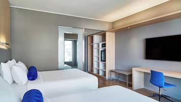 Habitación de hotel moderna con dos camas, un escritorio, una silla, un televisor y un armario.