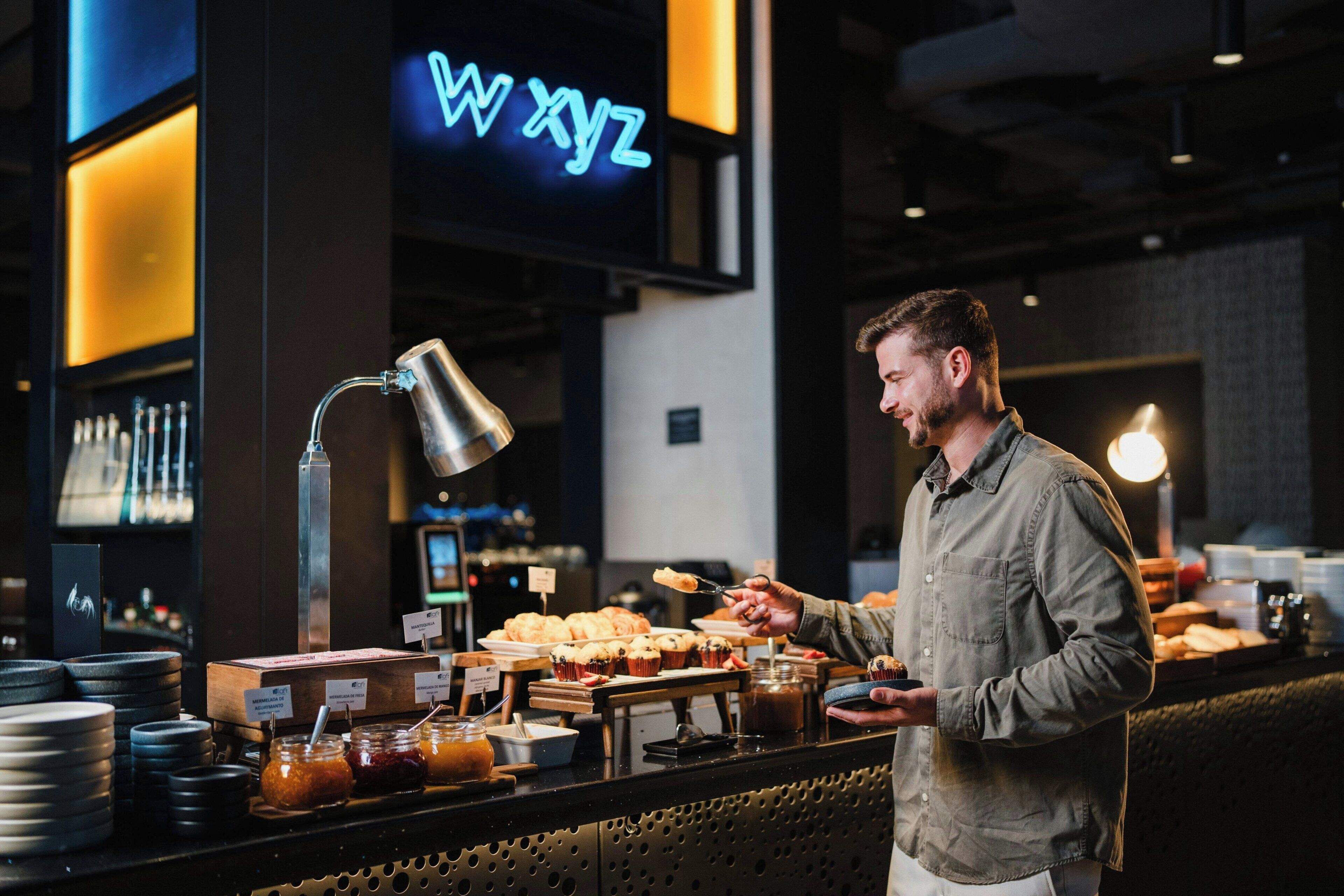 A person serving food at a counter with a neon sign in the background.