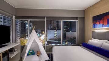 A hotel room with a large window, a bed, a TV, a white tent, and a city view.