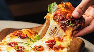 A hand pulling a slice of pizza with cheese and toppings from a wooden board.