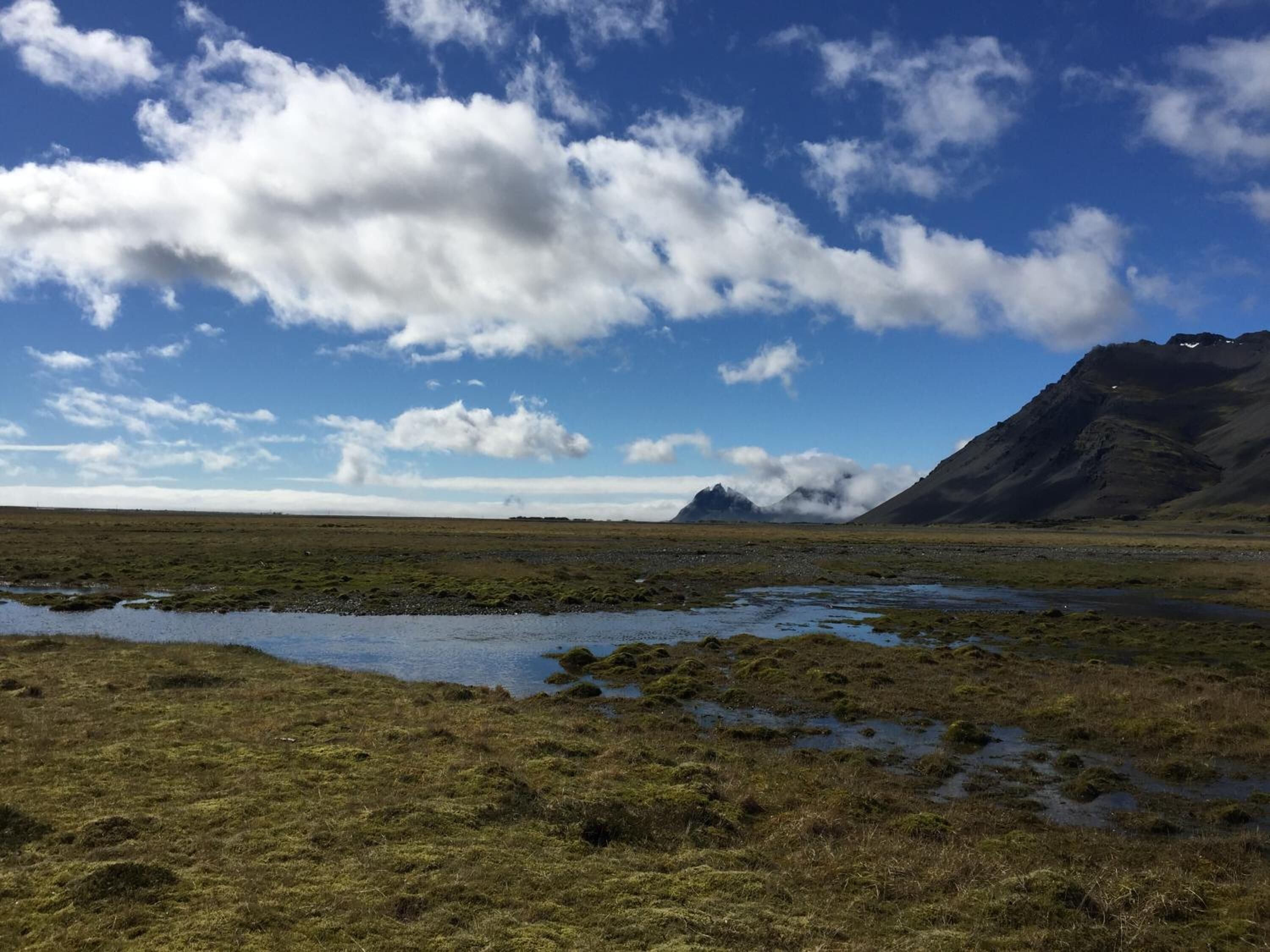 Un paysage naturel caractérisé par un terrain plat, un petit plan d’eau et une montagne en arrière-plan.