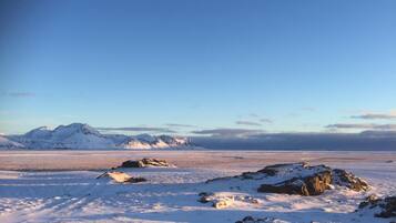 A snowy landscape with mountains in the background and rocks in the foreground.