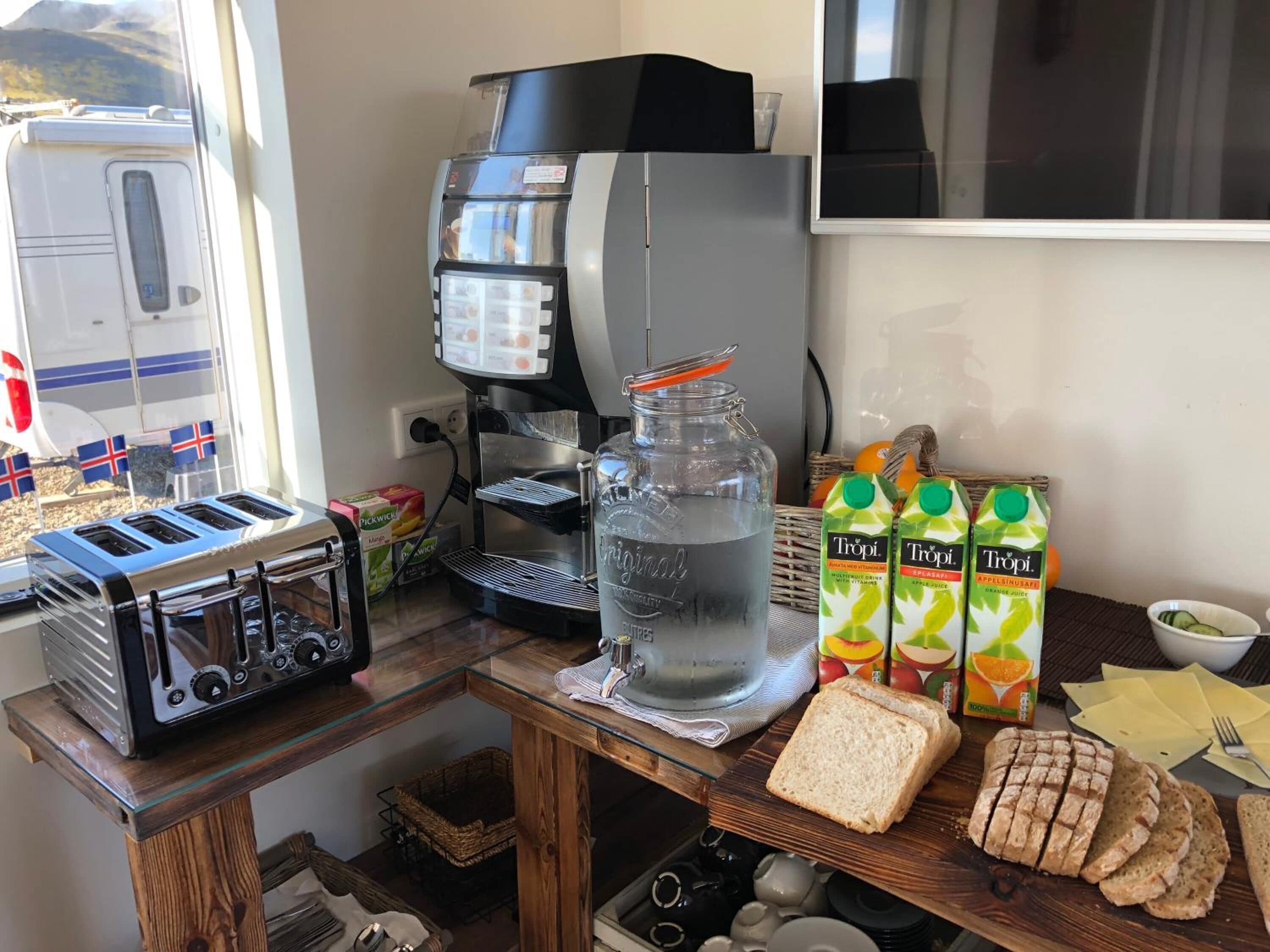 Una encimera de cocina con cafetera, tostadora, jarra de agua y cartones de jugo.