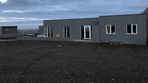 A modern building with large windows and a flat roof, situated on a gravel surface. - Hrafnavellir Guest House (Höfn)