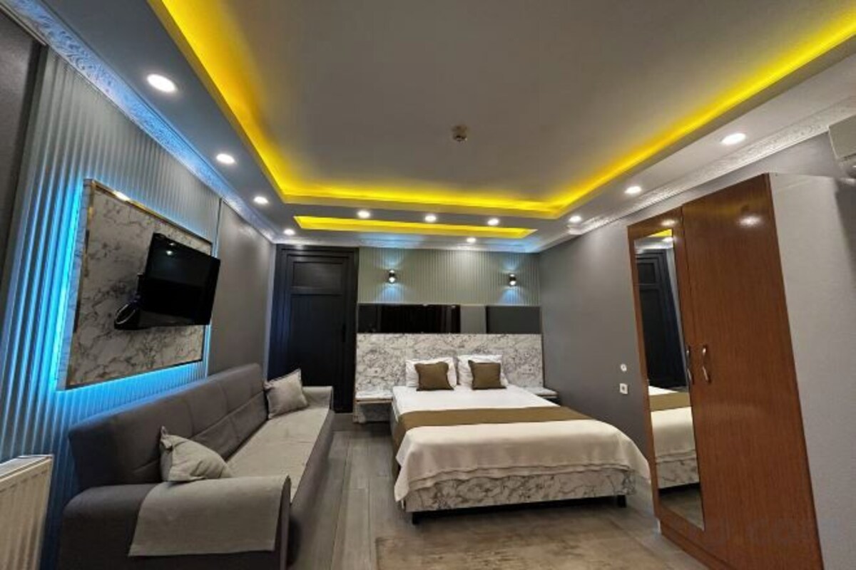 A modern bedroom with a sofa, a bed, and a TV mounted on the wall.