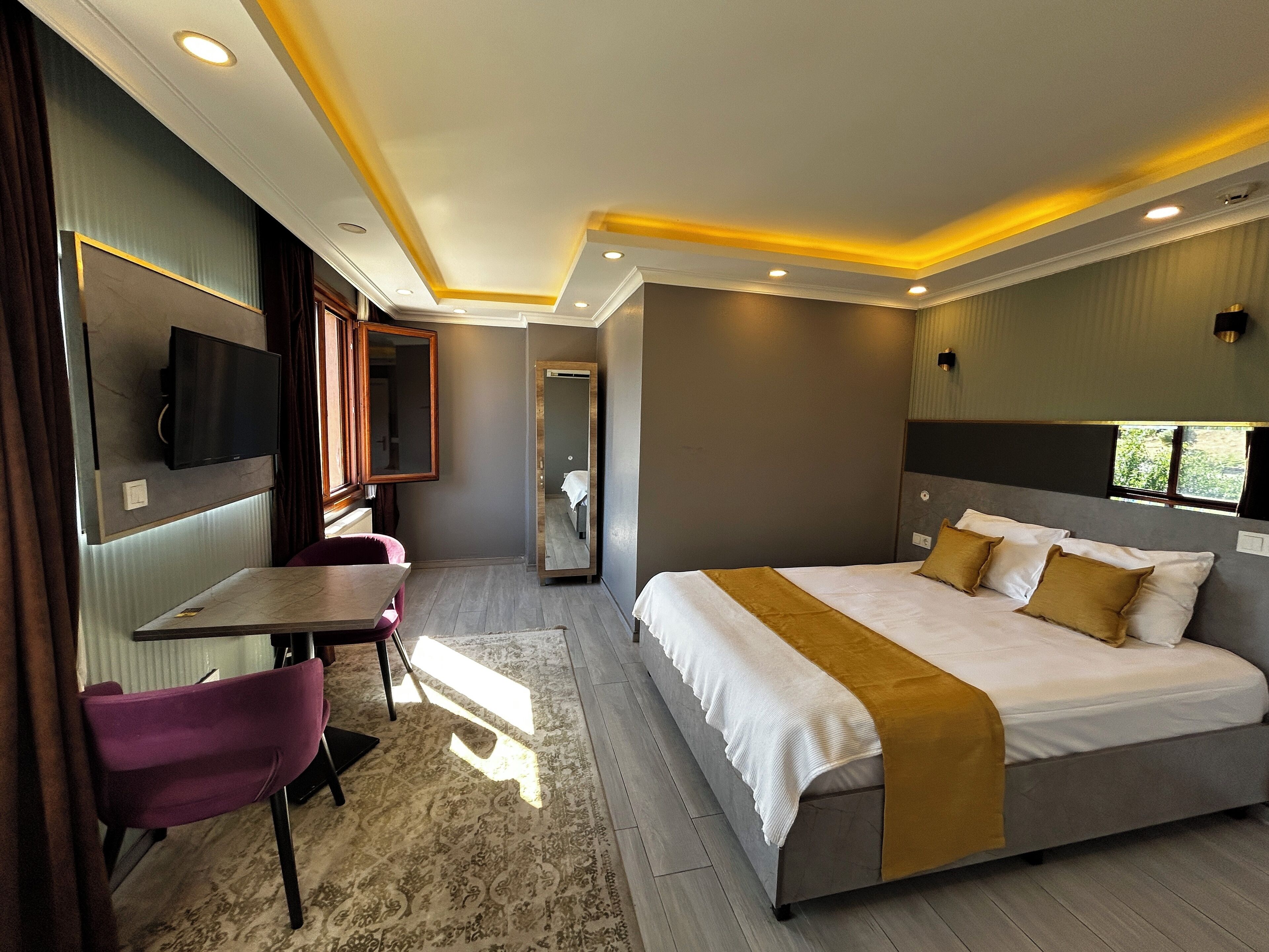 Quarto de hotel moderno com uma cama grande, uma escrivaninha, uma cadeira, uma TV fixada na parede e um espelho.